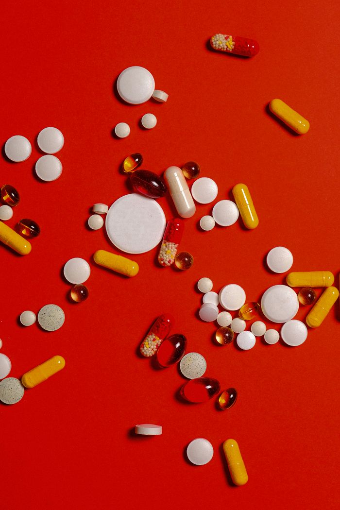 A diverse array of pills and capsules scattered on a vibrant red surface.
